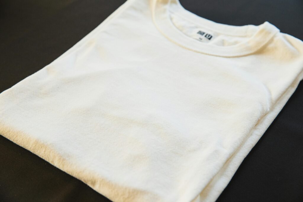 Un t-shirt blanc plié posé sur une surface sombre, mettant en valeur une mode minimaliste.