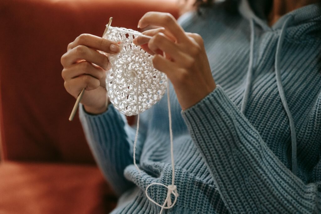 Une vue rapprochée des mains tricotant avec une aiguille au crochet tout en portant un pull bleu à l'intérieur.